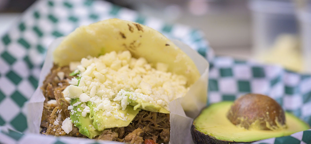 Arepa rellena de queso, carne y aguacate, acompañado de medio aguacate, sobre una servilleta de cuadros.