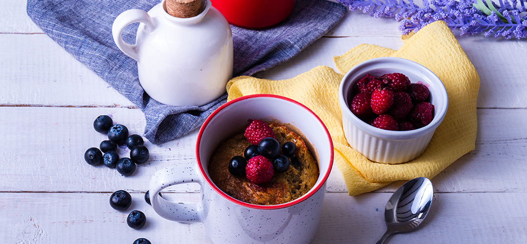 Postre con frutos rojos, servido en diferentes recipientes. Alrededor hay dos servilletas y una cuchara. Todo sobre una mesa de madera.